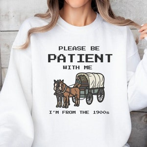 May include: White sweatshirt with a graphic of a horse-drawn wagon and the text "Please be patient with me I'm from the 1900s".