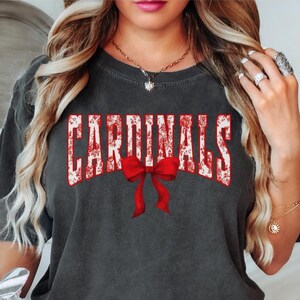 Cardinals School team spirit shirt that has a cute trendy coquette bow graphic in the collegiate lettering that says cardinals perfect for college football season and basketball and also high school mascot shirts and sports moms that like to show school spirit
