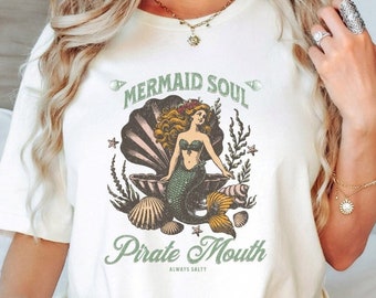 May include: White t-shirt with a vintage illustration of a mermaid in a seashell with the text "Mermaid Soul Pirate Mouth Always Salty".