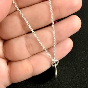 May include: A silver-toned metal chain necklace featuring a simple, circular pendant attached to the chain by a small jump ring. The chain consists of delicate, interlocking oval links that create a continuous, lightweight, and reflective silver-colored strand.