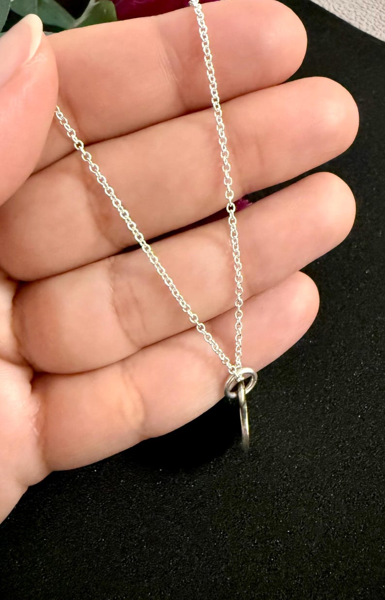 May include: A silver-toned metal chain necklace featuring a simple, circular pendant attached to the chain by a small jump ring. The chain consists of delicate, interlocking oval links that create a continuous, lightweight, and reflective silver-colored strand.