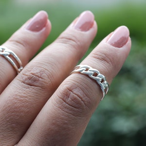 Pode incluir: Um anel de corrente de prata em um dedo com esmalte de unha rosa claro.