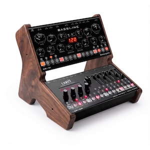 May include: A dual-tier synthesizer stand crafted from dark wood, holding two black electronic music devices. The top unit is labeled BASSLINE with a red digital display showing 120. The bottom unit is labeled LXR-02 with multiple knobs and buttons.