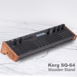 Può includere: Un sintetizzatore Korg SQ-64 nero su un supporto in legno. Il supporto è in legno marrone chiaro e ha una forma triangolare.