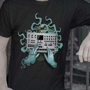 May include: A black t-shirt with a graphic design of a synthesizer with two green hands reaching out to touch the buttons. The design is surrounded by a green, swirling pattern.