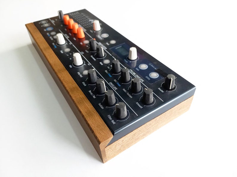 May include: A black synthesizer with a wooden side panel. The synthesizer has a digital display, knobs, and buttons. The text "Cycling Envelope" is visible on the front panel.