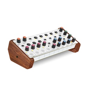May include: A white synthesizer with a wooden case. The synthesizer has a grid of knobs with different colors, including red, blue, green, and black.