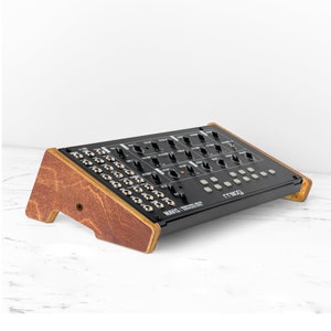 May include: A black Moog Mavis Synthesizer with a wooden stand. The synthesizer has a row of knobs and buttons, and a row of jacks on the front panel. The text "MAVIS" and "SYNTHESIZER" is printed on the front panel.