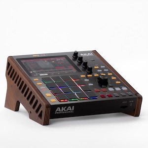 Puede incluir: Un centro de producción musical Akai MPC One negro con un soporte de madera. El dispositivo tiene una pantalla, perillas, botones y una cuadrícula de pads iluminados. El logotipo de Akai Professional es visible.