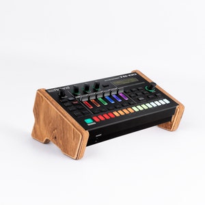 Peut inclure: Une boîte à rythmes Roland TR-8S Rhythm Performer noire avec un support en bois. La boîte à rythmes possède une variété de boutons et de molettes, y compris un grand écran LCD qui affiche le motif rythmique actuel.