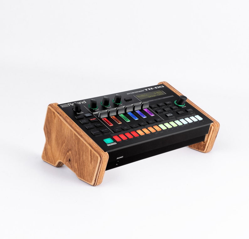 K&ouml;nnte beinhalten: Eine schwarze Roland TR-8S Rhythm Performer Drum Machine mit einem Holzst&auml;nder. Die Drum Machine verf&uuml;gt &uuml;ber eine Vielzahl von Kn&ouml;pfen und Reglern, darunter ein gro&szlig;es LCD-Display, das das aktuelle Rhythmusmuster anzeigt.