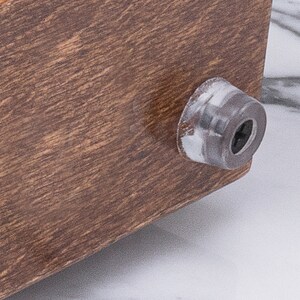 May include: A close-up of a wooden table leg with a brown finish. The leg has a round, gray plastic foot.