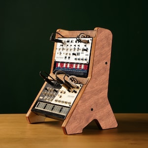 May include: A wooden stand holding three electronic music synthesizers. The stand is made of light brown wood and has a unique angled design. The synthesizers are white and black with various knobs and buttons. Cables are plugged into the synthesizers.