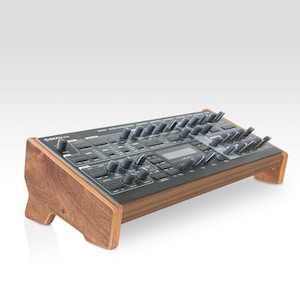 以下が含まれることがあります： 木製のスタンドが付いた黒いシンセサイザー。シンセサイザーには、さまざまなノブやボタン、小さなLCDスクリーンがあります。