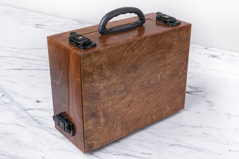 Peut inclure: Une bo&icirc;te de transport en bois avec une finition teint&eacute;e brune et une poign&eacute;e en plastique noir. La bo&icirc;te a deux loquets noirs de chaque c&ocirc;t&eacute;.