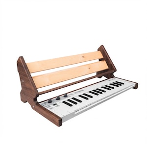 May include: A wooden keyboard stand featuring dark brown side panels and two light-colored horizontal slats, holding a white MIDI keyboard controller with black and white keys, various control knobs, and buttons on its top surface.