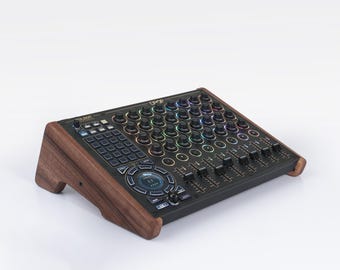 Puede incluir: Un mezclador de audio negro con numerosas perillas, botones y controles deslizantes. El mezclador tiene un marco de madera y está sobre un fondo blanco. La parte superior del mezclador tiene una cuadrícula de luces multicolores.