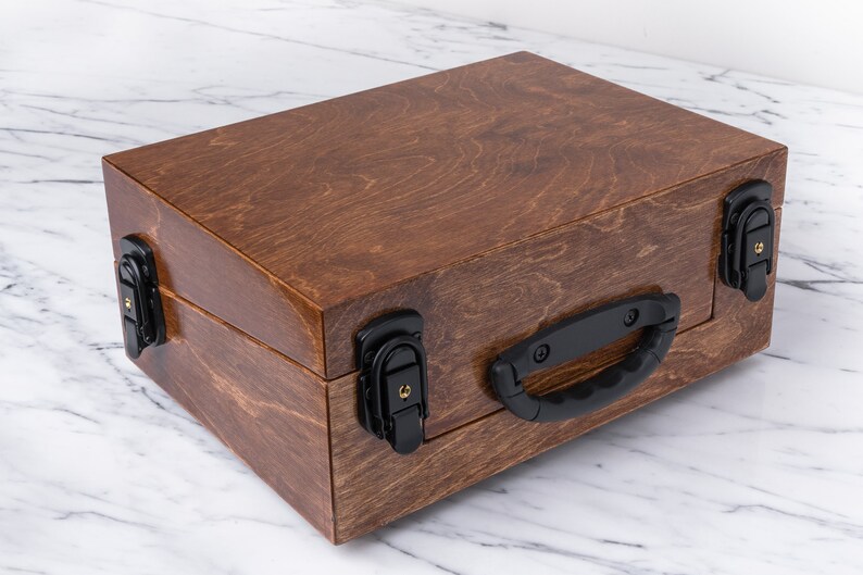 Peut inclure: Une bo&icirc;te en bois avec une finition teint&eacute;e brune. La bo&icirc;te a une poign&eacute;e noire et quatre fermoirs noirs.