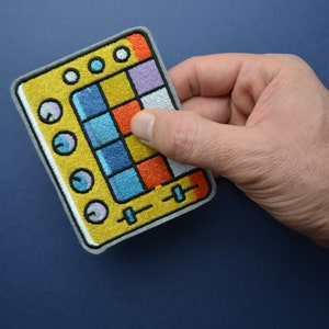 May include: A yellow and blue embroidered patch of a music sampler with knobs and sliders.