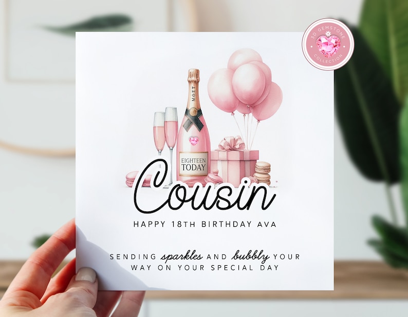 May include: Pink birthday card with a bottle of champagne, glasses, macarons, and balloons. The card says "Cousin Happy 18th Birthday Ava Sending sparkles and bubbly your way on your special day"