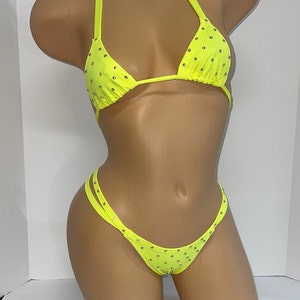 Könnte beinhalten: Neongelbes Bikini-Set mit Strasssteinen. Das Triangel-Oberteil hat Neckholder-Träger, und das Höschen hat ein Doppelriemen-Design. Die Bademode wird auf einer Schaufensterpuppe vor weißem Hintergrund präsentiert.