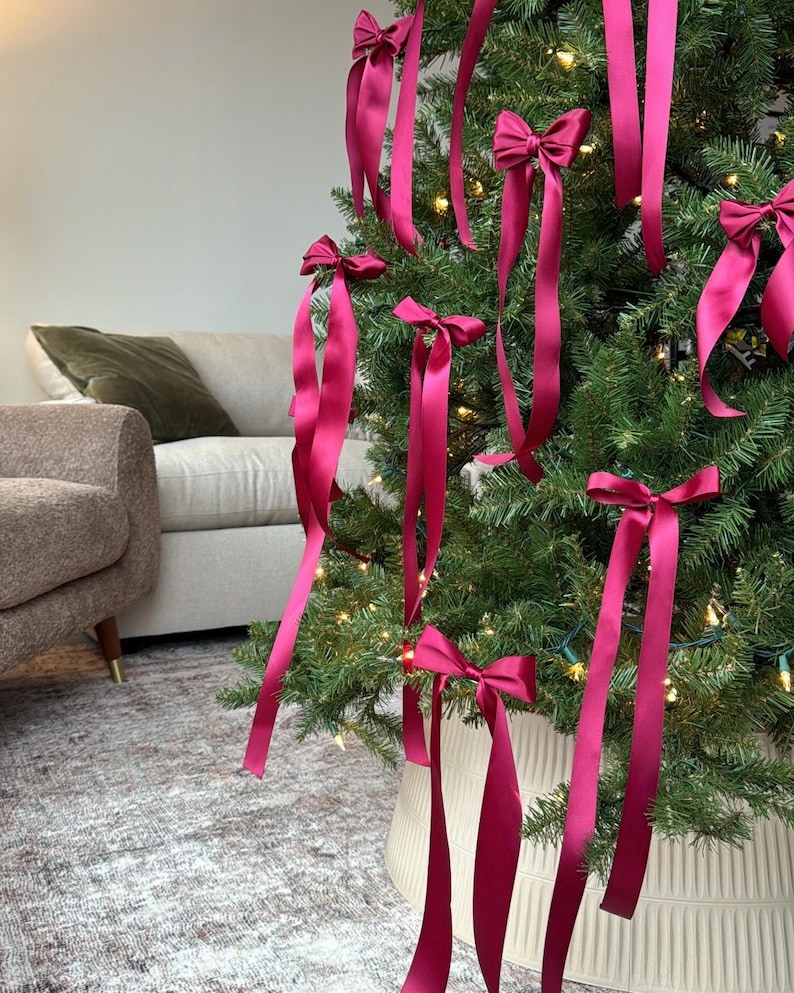 May include: A Christmas tree decorated with burgundy satin ribbon bows. The tree is in a burgundy planter with a ribbed design.