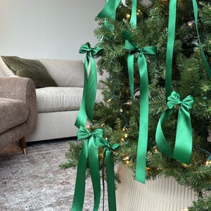 May include: A green Christmas tree decorated with green satin ribbon bows. The tree is in a white planter with a textured surface.