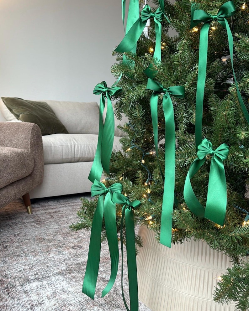 May include: A green Christmas tree decorated with green satin ribbon bows. The tree is in a white planter with a textured surface.