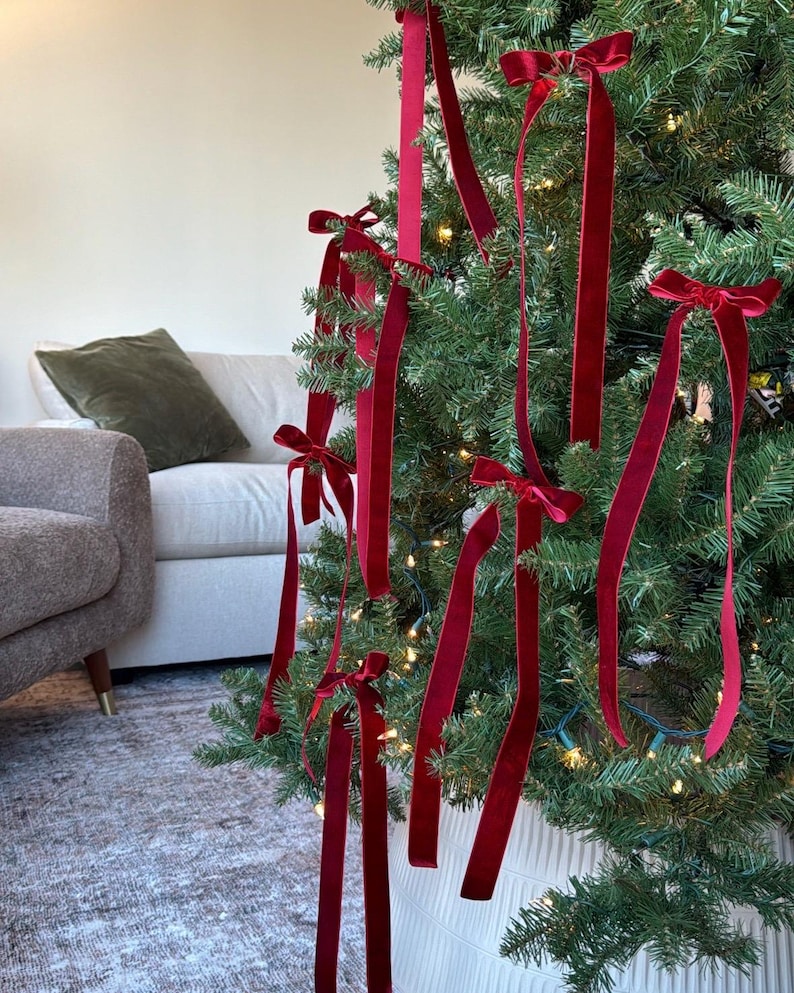 May include: A Christmas tree decorated with red velvet ribbon bows. The tree is lit with white fairy lights and is in a white planter.