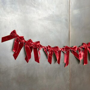 Puede incluir: Una guirnalda de lazos de terciopelo rojo enhebrados. Los lazos est&aacute;n atados con una cinta dorada.