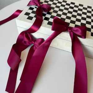 May include: Three burgundy satin ribbon bows tied on a black and white checkered box. The box is made of white marble with black squares.