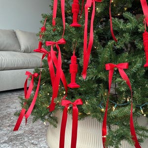 May include: A Christmas tree decorated with red velvet nutcracker ornaments and red satin ribbon bows. The tree is in a white planter with a textured design.