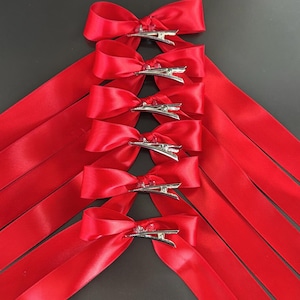 May include: Set of six red satin ribbon hair bows with silver clips. Each bow is tied with a simple knot and has a long ribbon tail.