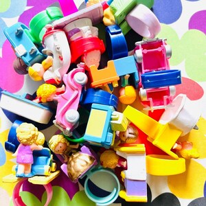Może przedstawiać: Kolekcja kolorowych plastikowych pierścieni z zabawkami przedstawiających różne postacie i pojazdy. Pierścienie są w jasnych kolorach, takich jak żółty, niebieski, różowy i zielony. Postacie obejmują dziewczynkę w różowej sukience, dziewczynkę w niebieskiej sukience, chłopca w niebieskiej koszuli i konia. Pojazdy obejmują samochód, ciężarówkę i łódź.