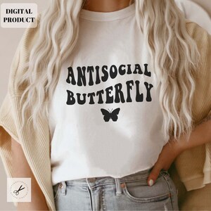 Puede incluir: Camiseta blanca con texto negro que dice "ANTISOCIAL BUTTERFLY" en una fuente retro. Un peque&ntilde;o gr&aacute;fico de mariposa negra se encuentra debajo del texto.