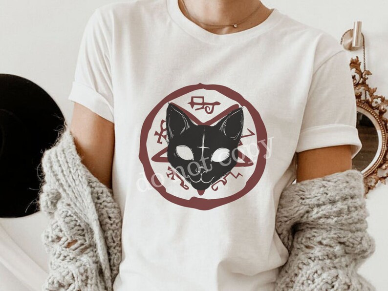 K&ouml;nnte beinhalten: Wei&szlig;es T-Shirt mit einer schwarzen Katzenillustration in einem roten Kreis mit einem Pentagramm und anderen Symbolen. Die Katze hat wei&szlig;e Augen und ein Kreuz auf der Stirn.