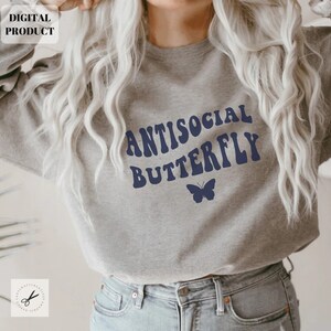 Puede incluir: Una sudadera gris con el texto "Antisocial Butterfly" en azul, con letras de estilo retro. Un peque&ntilde;o gr&aacute;fico de mariposa azul se encuentra debajo del texto.