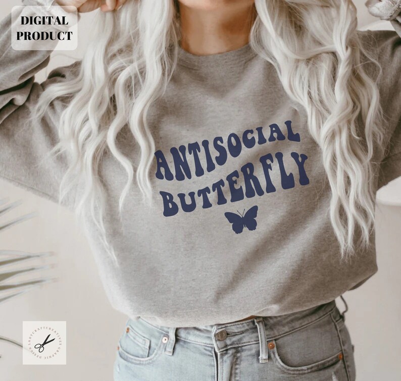 Puede incluir: Una sudadera gris con el texto "Antisocial Butterfly" en azul, con letras de estilo retro. Un peque&ntilde;o gr&aacute;fico de mariposa azul se encuentra debajo del texto.