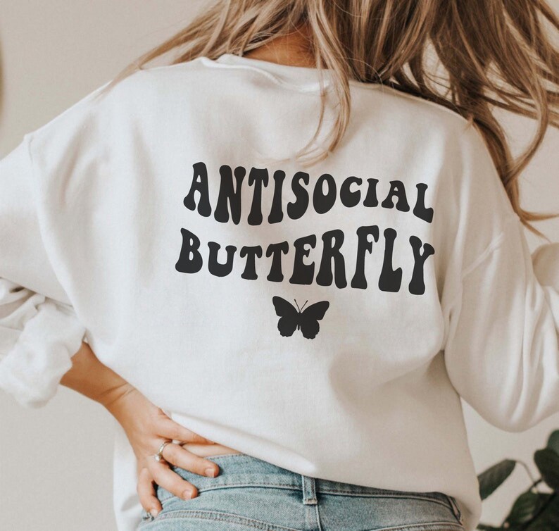 Puede incluir: Sudadera blanca con texto negro que dice "Antisocial Butterfly" en una fuente retro. Un peque&ntilde;o gr&aacute;fico de mariposa negra se encuentra debajo del texto.
