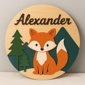 Könnte beinhalten: Runder Holzschild mit einem orange-weißen Cartoon-Fuchs, umgeben von grünen Bäumen und Bergen. Der Name "Alexander" ist in brauner Schrift geschrieben. Der Hintergrund ist helles Holz.