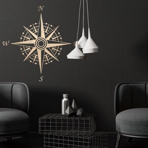 Puede incluir: Un dise&ntilde;o de br&uacute;jula negro y dorado en una pared negra con dos sillones negros y una mesa de metal negro con tapa de vidrio. El dise&ntilde;o de la br&uacute;jula tiene las letras N, S, E y W.