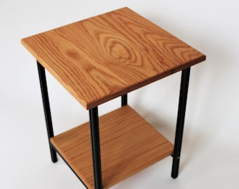 Puede incluir: Una pequeña mesa auxiliar de madera con un marco de metal negro. La mesa tiene una tapa cuadrada y un estante inferior.