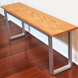 Puede incluir: Un banco de madera con un acabado de madera natural y un marco de metal plateado. El banco est&aacute; sentado en un suelo de madera dura.