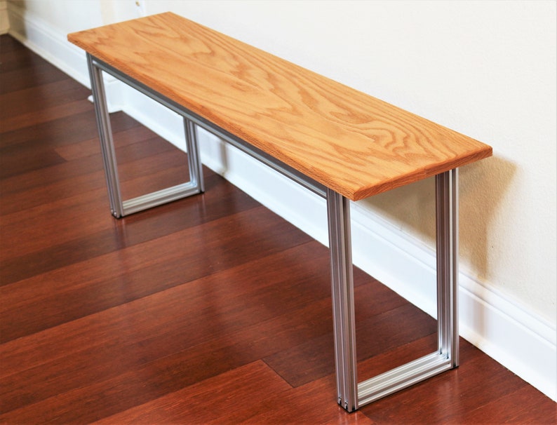 Puede incluir: Un banco de madera con un acabado de madera natural y un marco de metal plateado. El banco est&aacute; sentado en un suelo de madera dura.