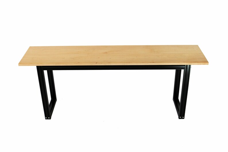 Puede incluir: Una mesa de madera larga y rectangular con un acabado de madera natural y patas de metal negro. La mesa est&aacute; sostenida por dos pares de patas, cada una con una forma rectangular.
