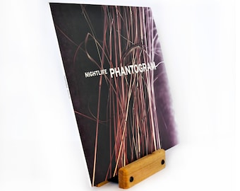 May include: A vinyl record stand made of wood with a dark brown finish. The stand is holding a vinyl record with a black and purple image of tall grass. The record cover has the text "NIGHTLIFE PHANTOGRAM" printed on it.