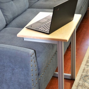 May include: A laptop computer sits on a light wood table with silver legs. The table is next to a blue couch.