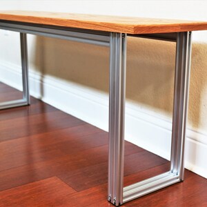 Puede incluir: Un banco de madera con un acabado de madera natural y patas de metal plateado. El banco est&aacute; sentado en un suelo de madera dura.