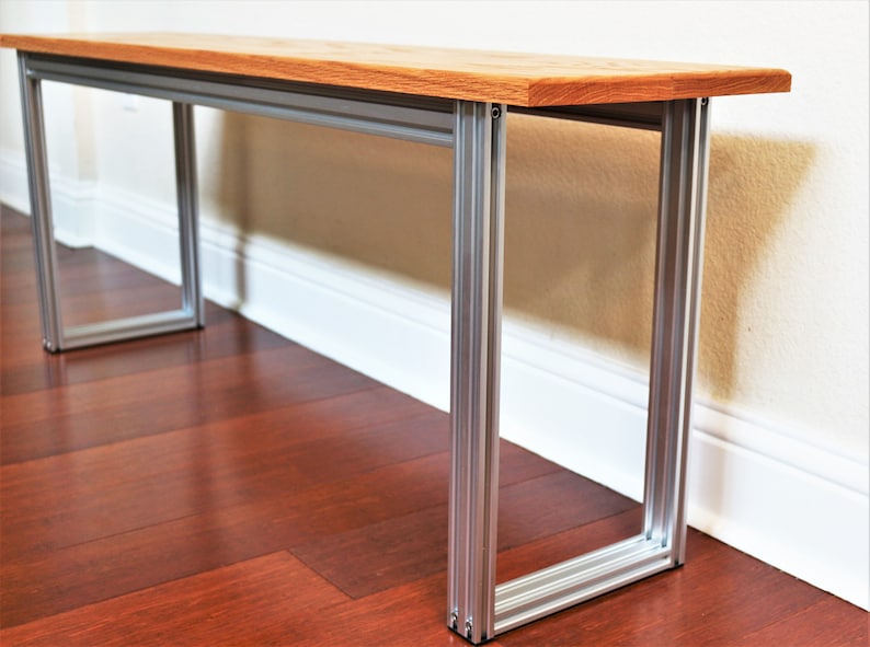 Puede incluir: Un banco de madera con un acabado de madera natural y patas de metal plateado. El banco est&aacute; sentado en un suelo de madera dura.