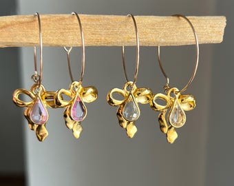 Creolen in Gold aus Edelstahl mit goldenen Schleifen und tropfenförmigen Charms in Rosa oder Transparent